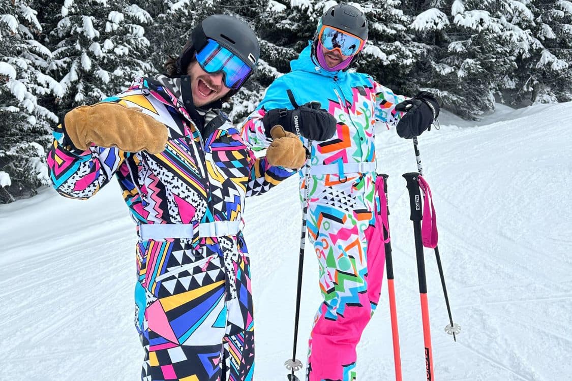 Two skiers in colorful OOSC ski suits posing for a photo.